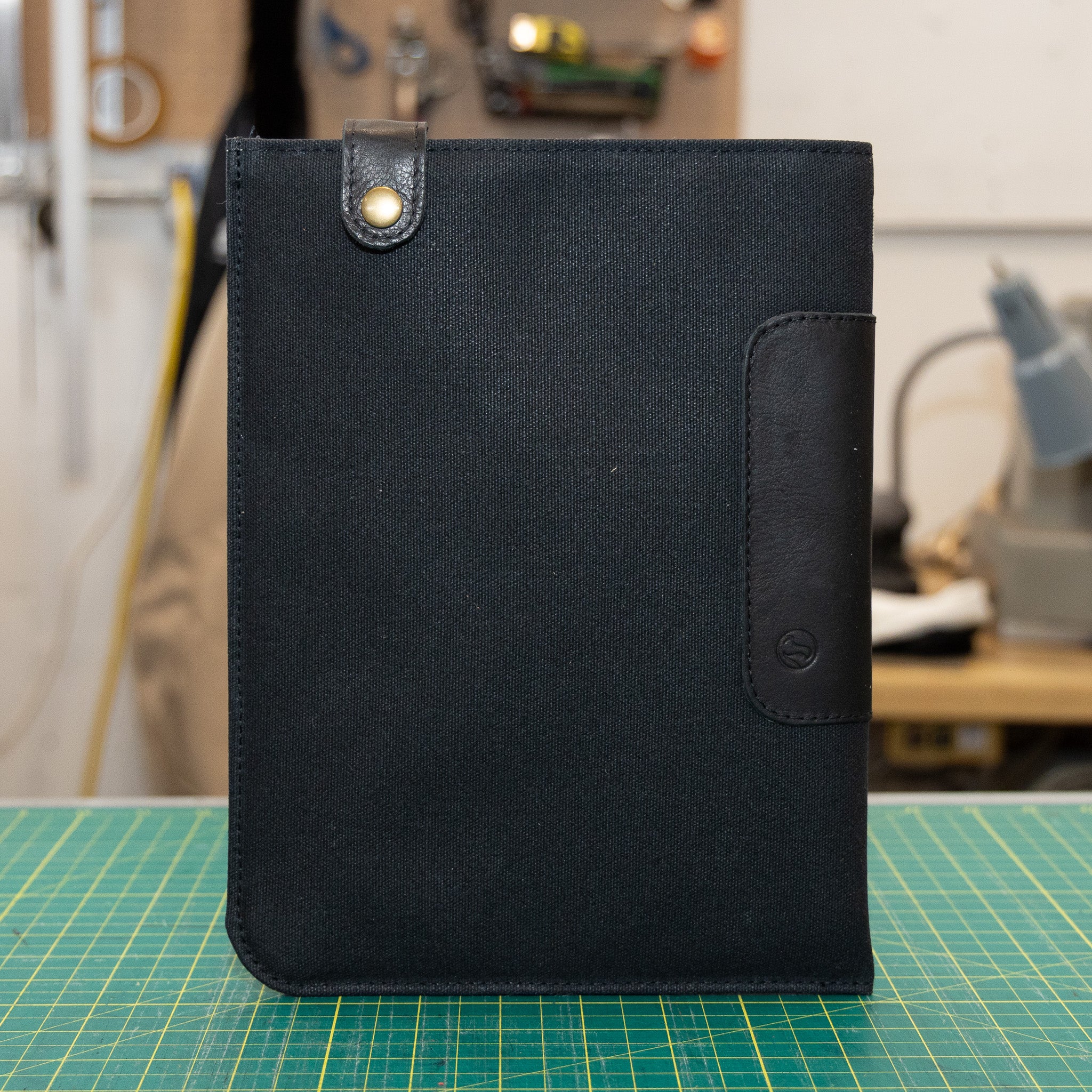 Black waxed canvas iPad sleeve on a green cutting mat with a workshop background