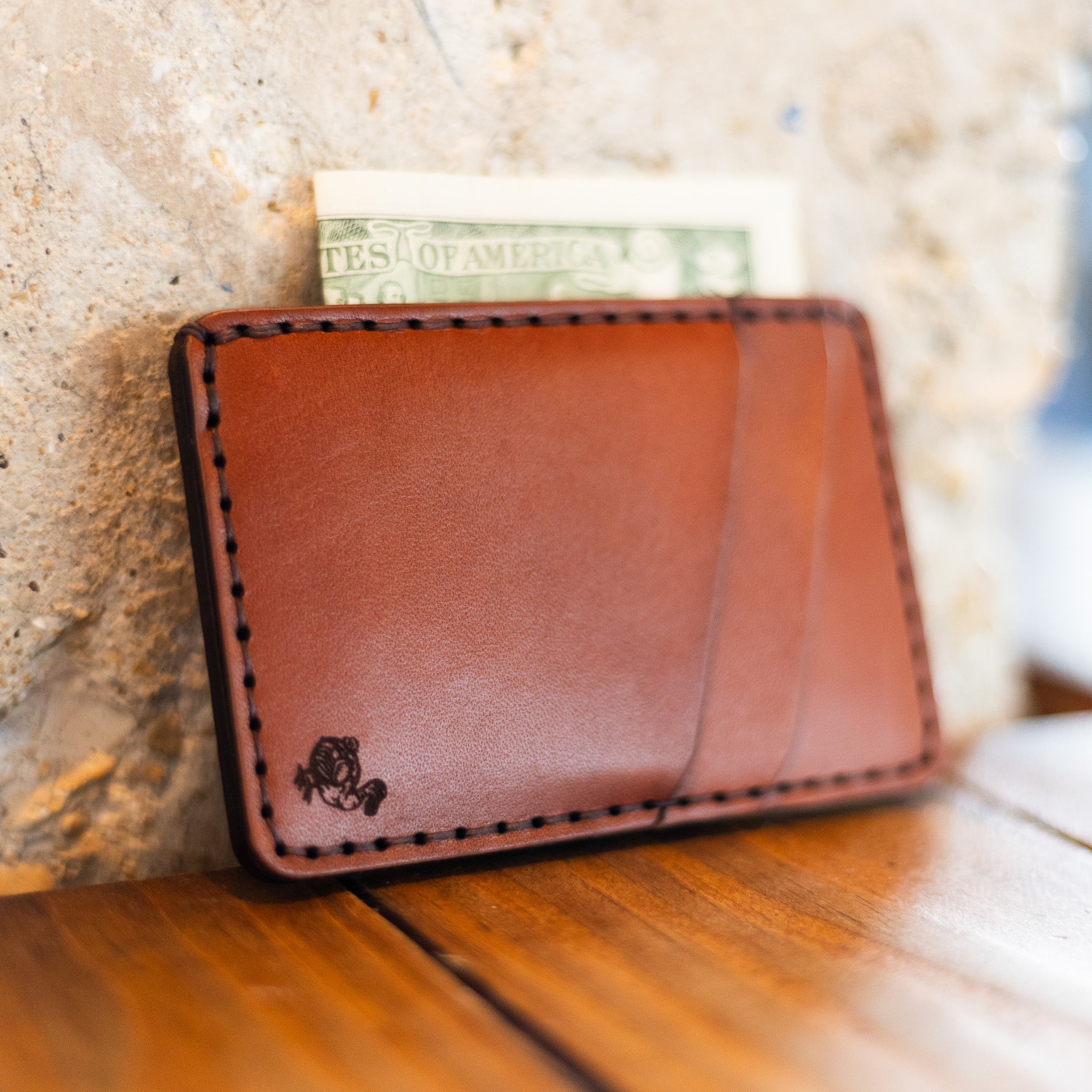 Leather front pocket wallet leaning on stone with cash and card