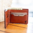 Leather bifold wallet open with cards and cash, lifestyle shot on wood table