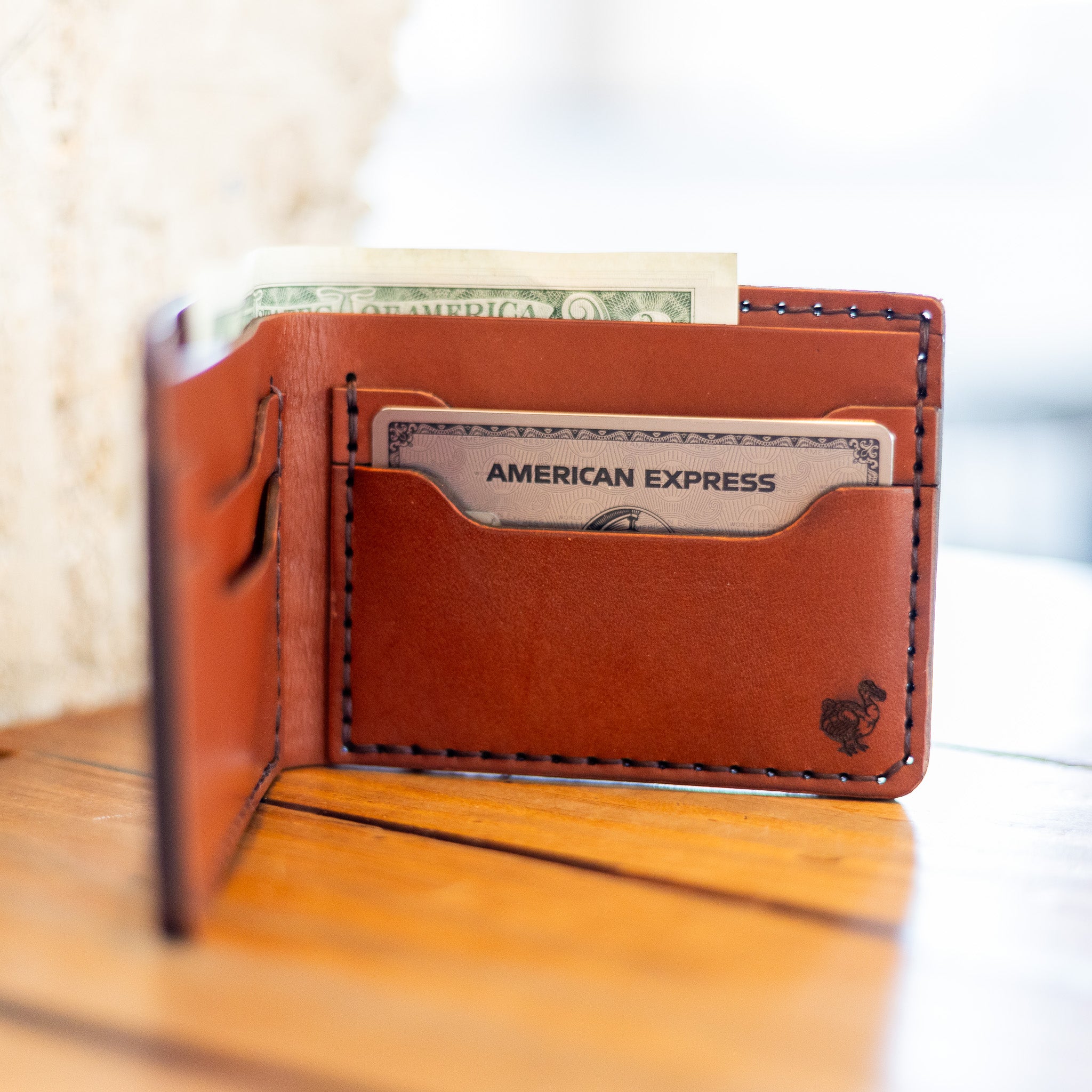 Leather bifold wallet open with cards and cash, lifestyle shot on wood table
