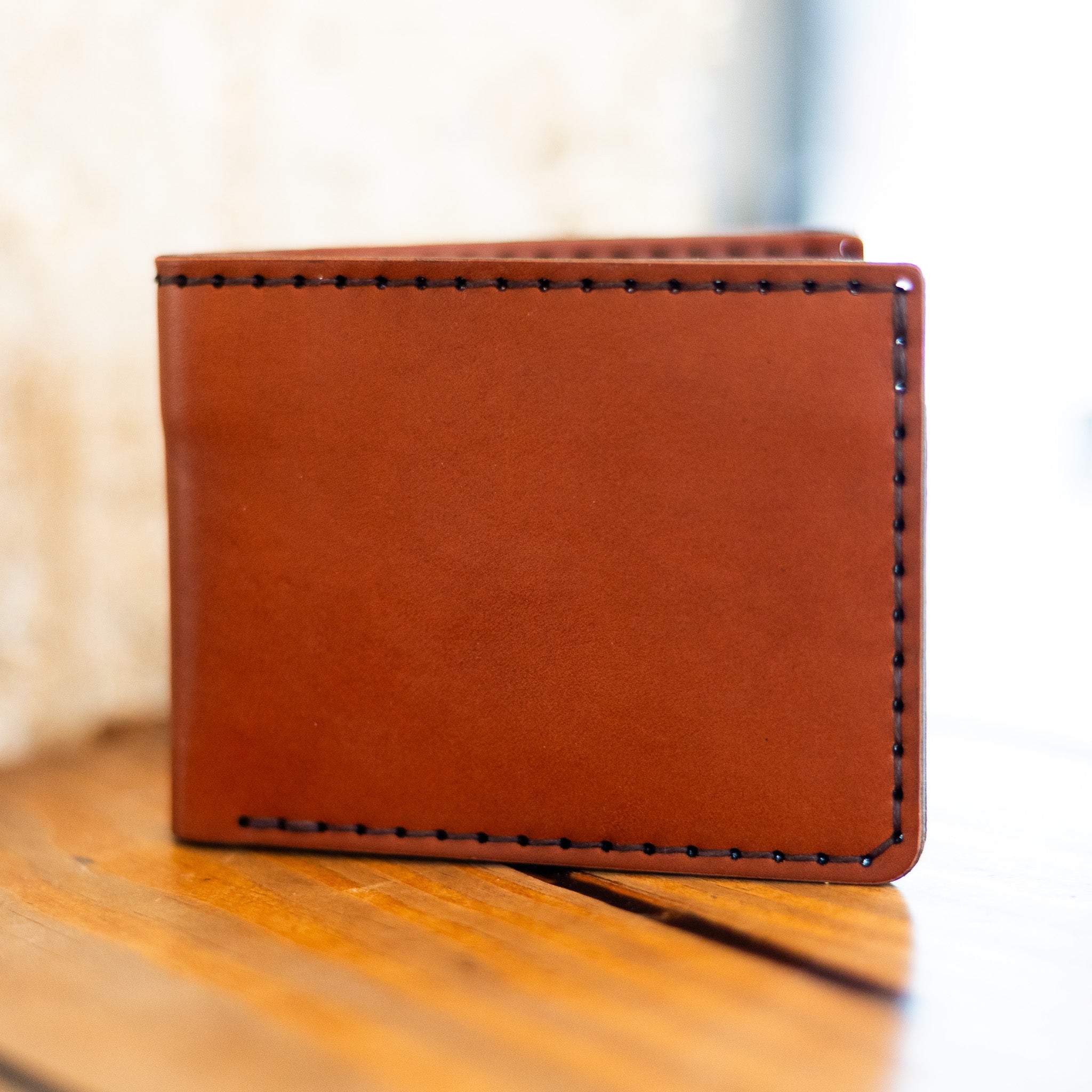 Chestnut leather bifold wallet closed, saddle stitched edges