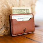 Chestnut leather card holder leaning on stone with card and bill