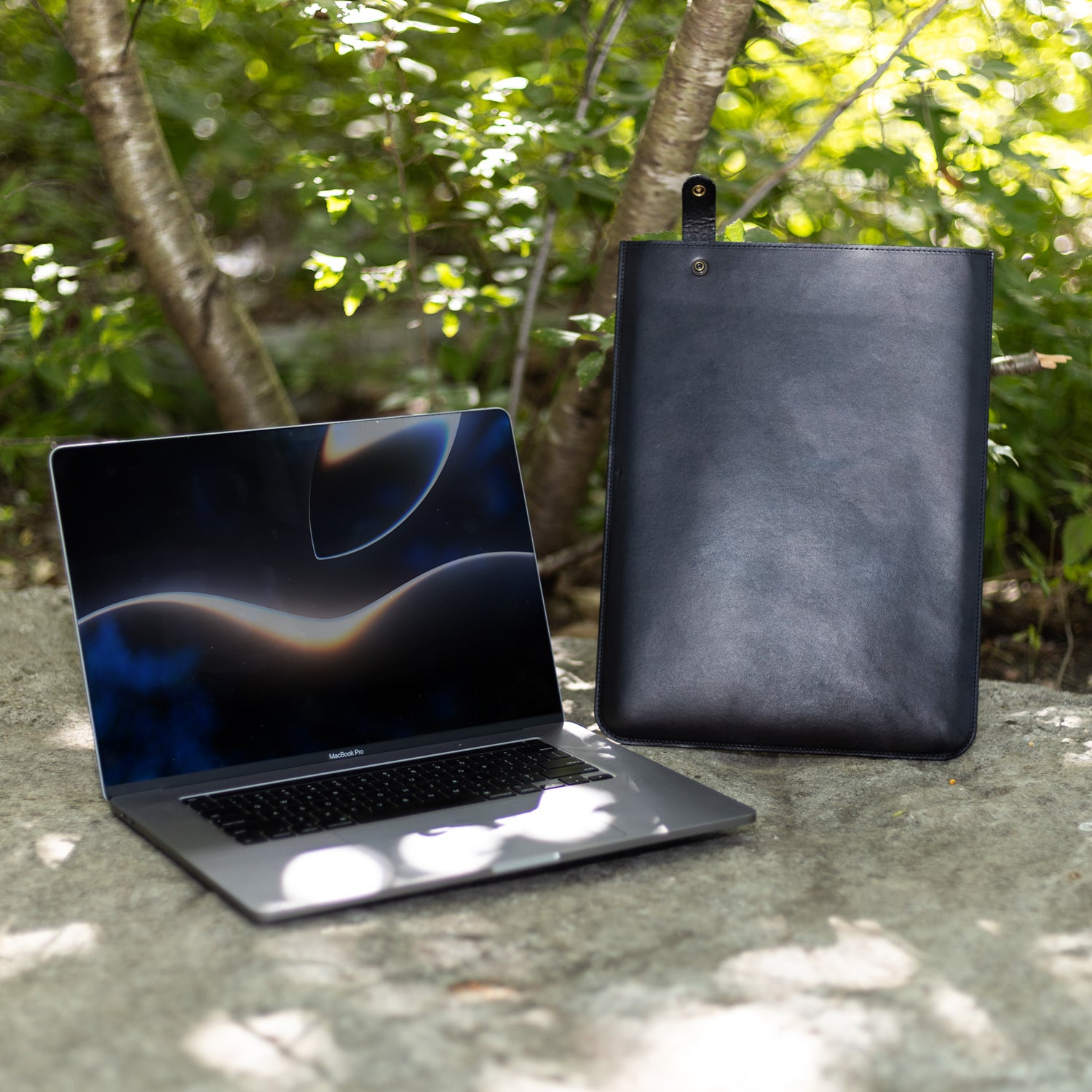 Black leather MacBook sleeve beside an open MacBook Pro