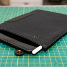 Black iPad Sleeve with waxed canvas with a iPad and white stylus on a green cutting mat