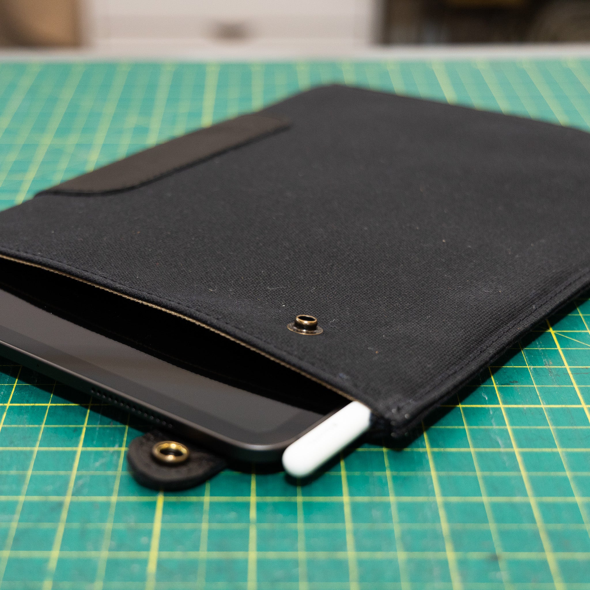 Black iPad Sleeve with waxed canvas with a iPad and white stylus on a green cutting mat