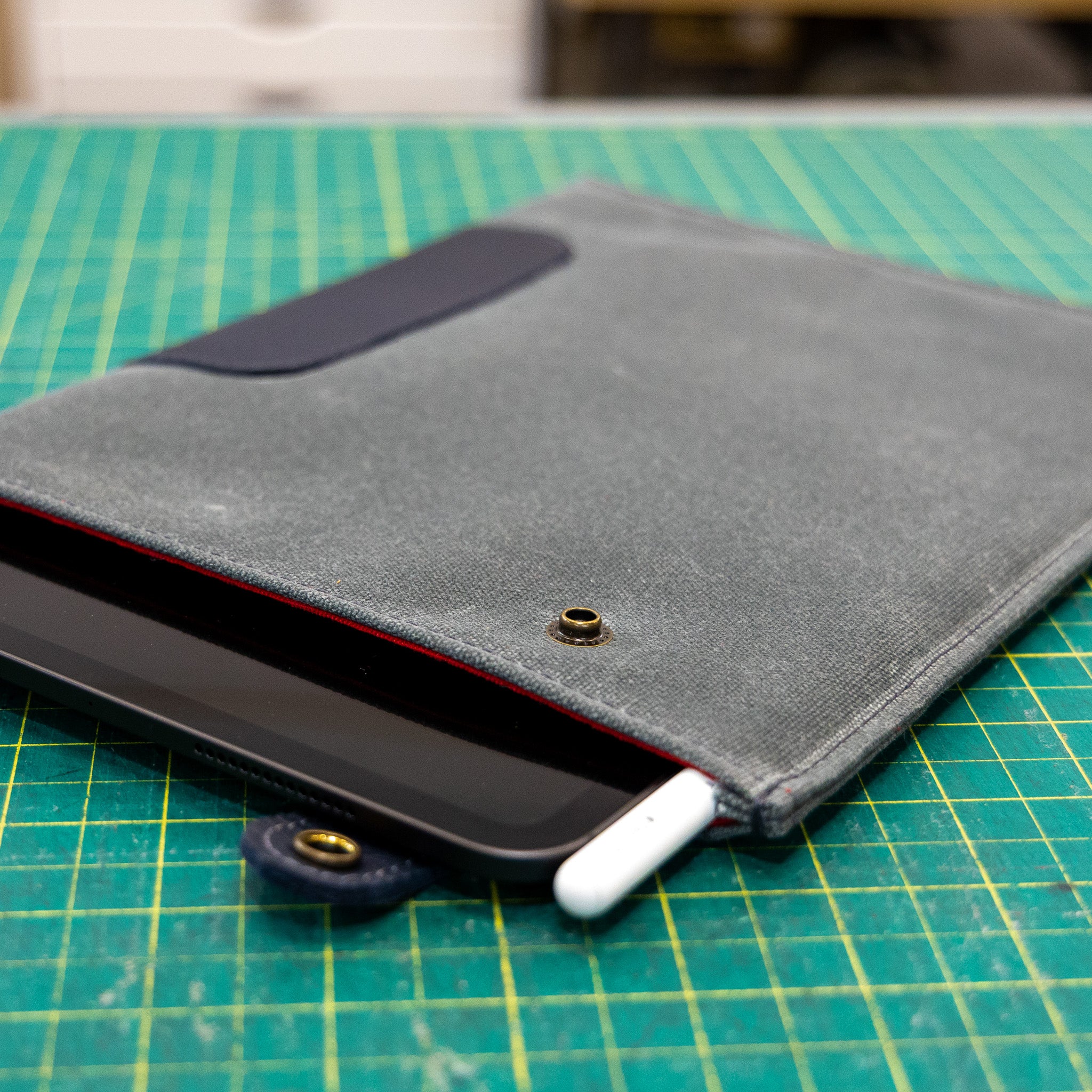 Blue iPad Sleeve with waxed canvas with a iPad and white stylus on a green cutting mat